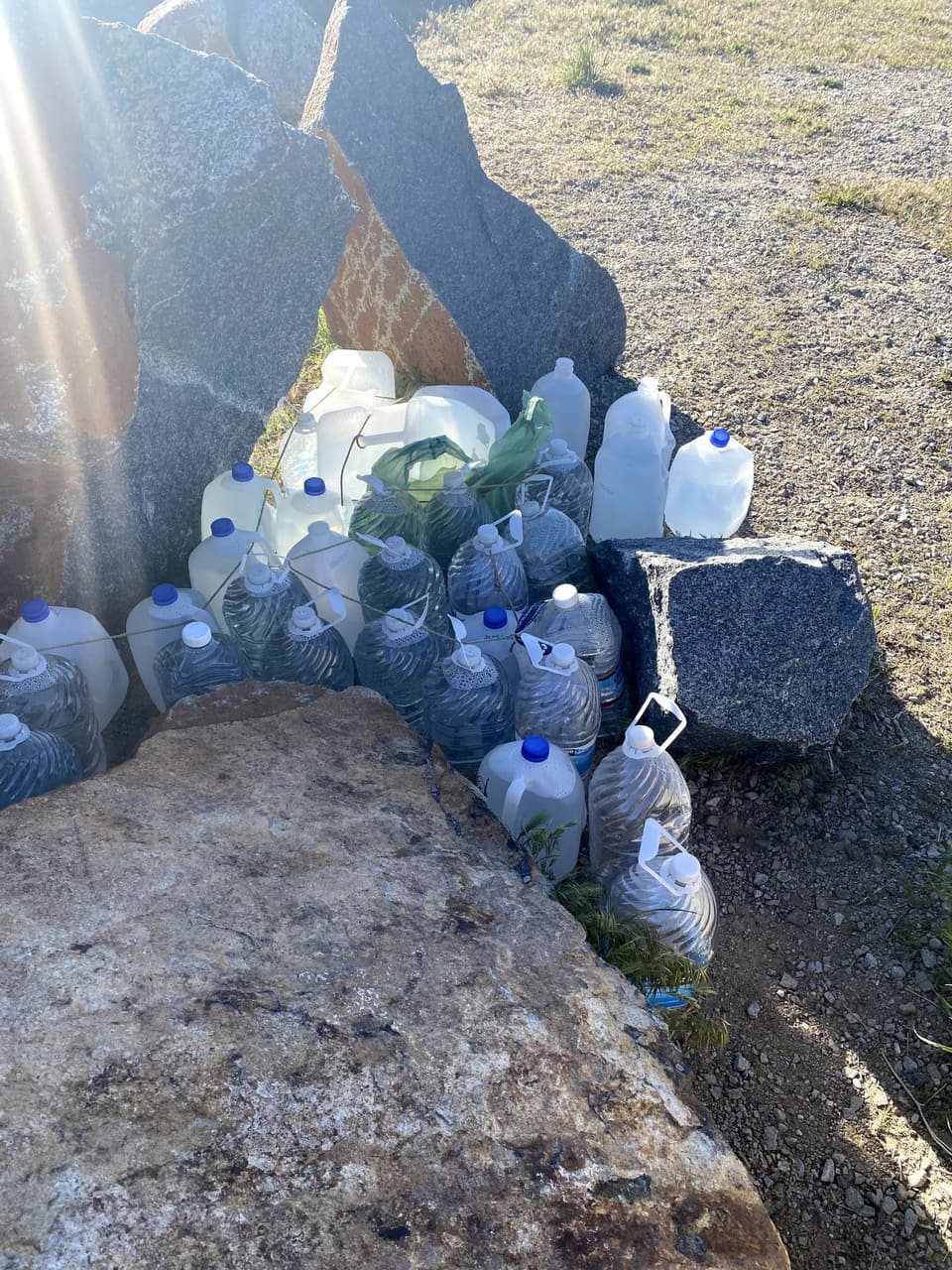 Gallon water jugs stacked among desert rocks at a trail cache